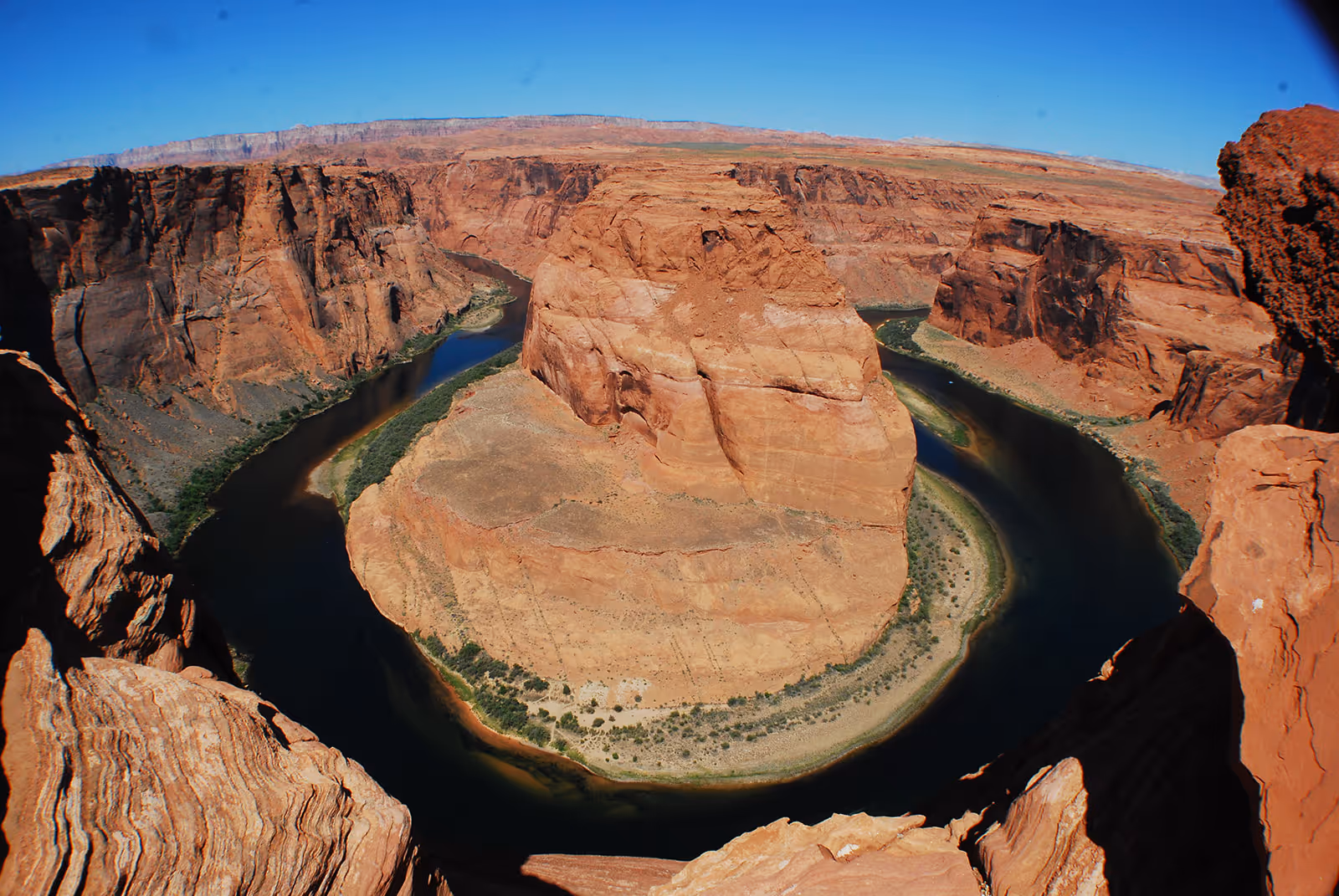 Wide aerial view of Horseshoe Bend showing a river curving around a large rock formation in a canyon under a clear blue sky.