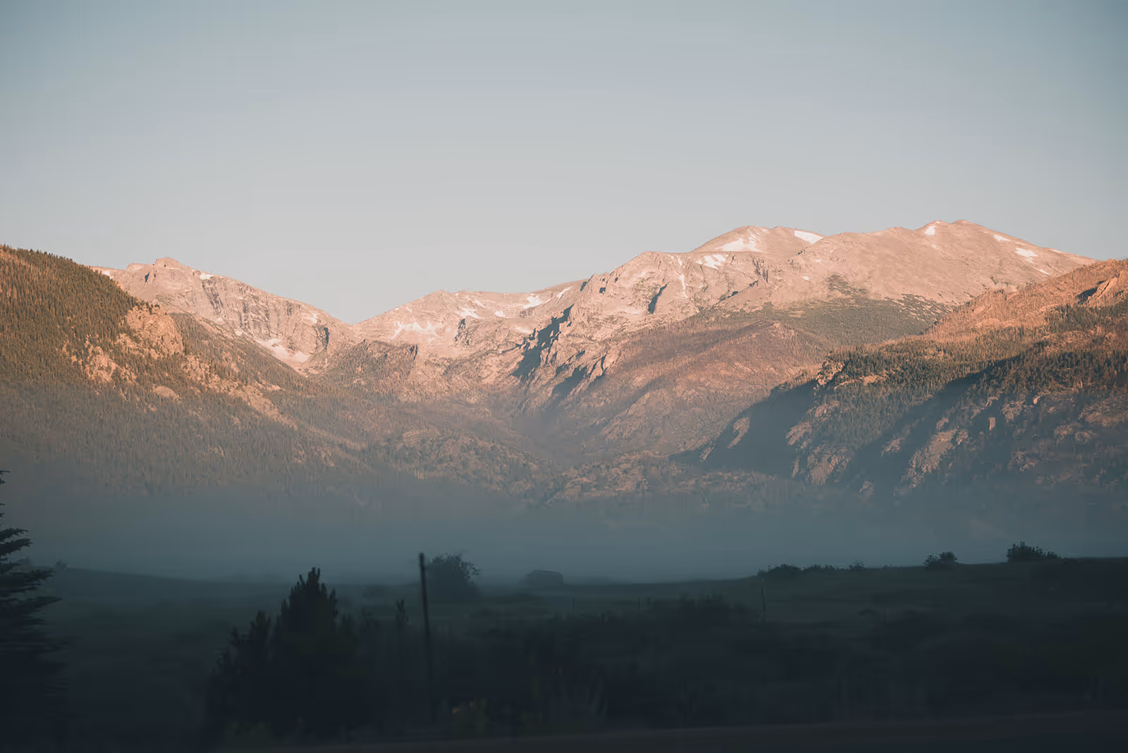 Mountain range with rocky peaks and patches of snow above a valley shrouded in mist during early morning or evening light.