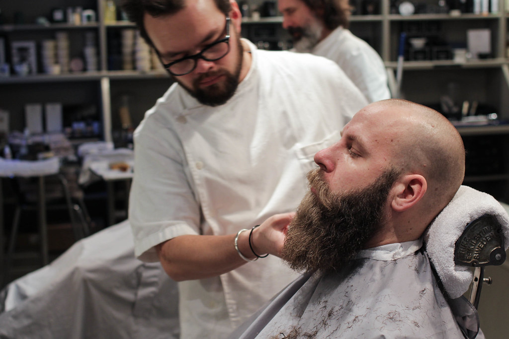 A barber shaving a bald man's beard