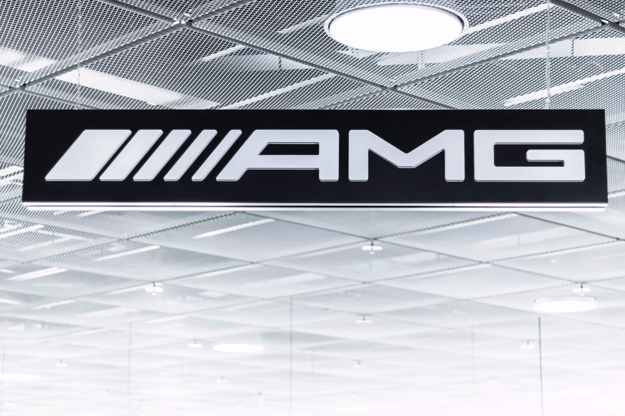 Illuminated AMG logo sign hanging from a ceiling with a mesh and grid pattern.