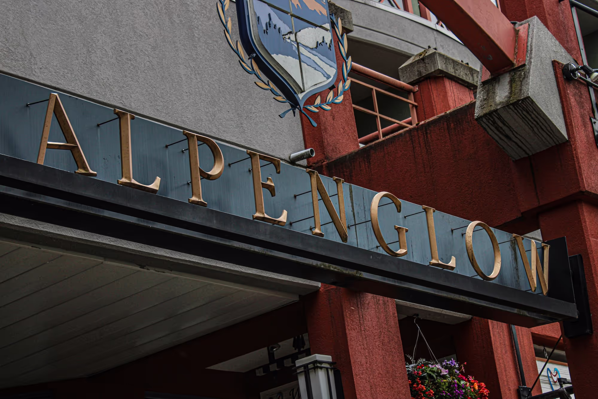 Close-up of a building sign with gold letters spelling 'ALPENGLOW' against a gray and red architectural background.