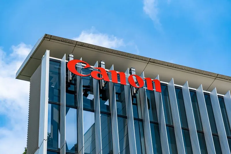 Canon company name in large red letters on modern glass building facade under a blue sky.