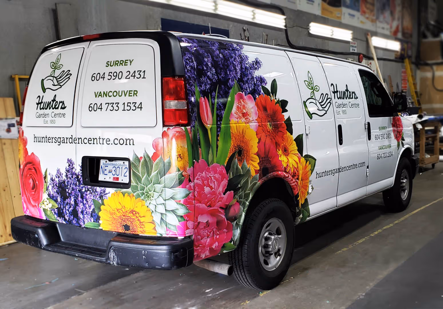 White delivery van with colorful flowers graphics and contact info for Hunters Garden Centre parked indoors.