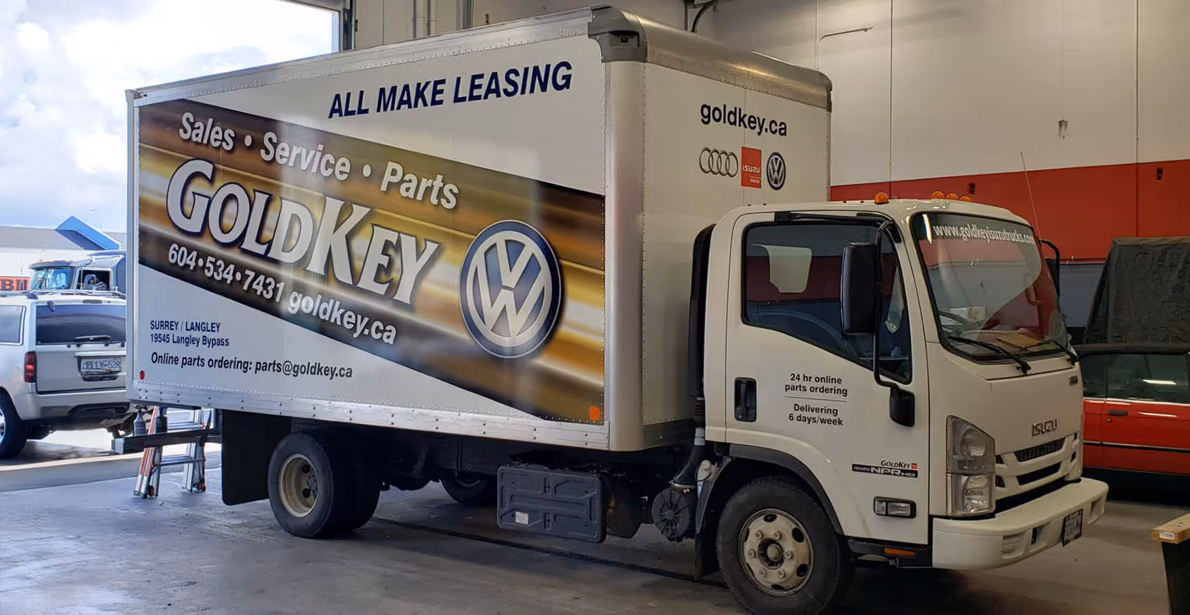 White Isuzu box truck with GoldKey auto service advertisement, parked inside a garage.