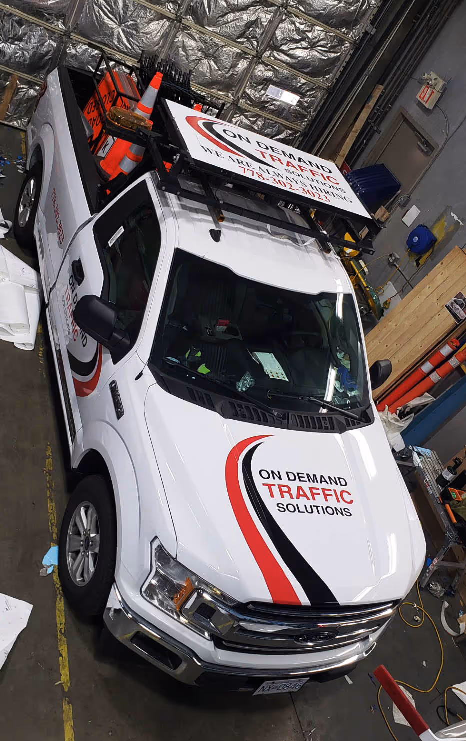 White pickup truck with On Demand Traffic Solutions branding and traffic cones in the bed, parked inside a garage.