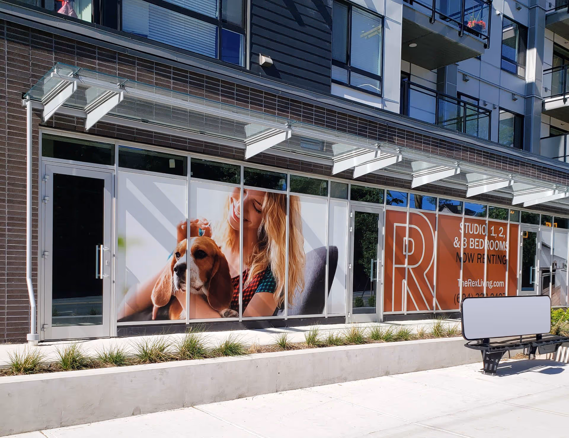 Apartment building storefront with window advertisements featuring a woman petting a dog and a sign for studio, 1, 2, and 3 bedroom rentals.