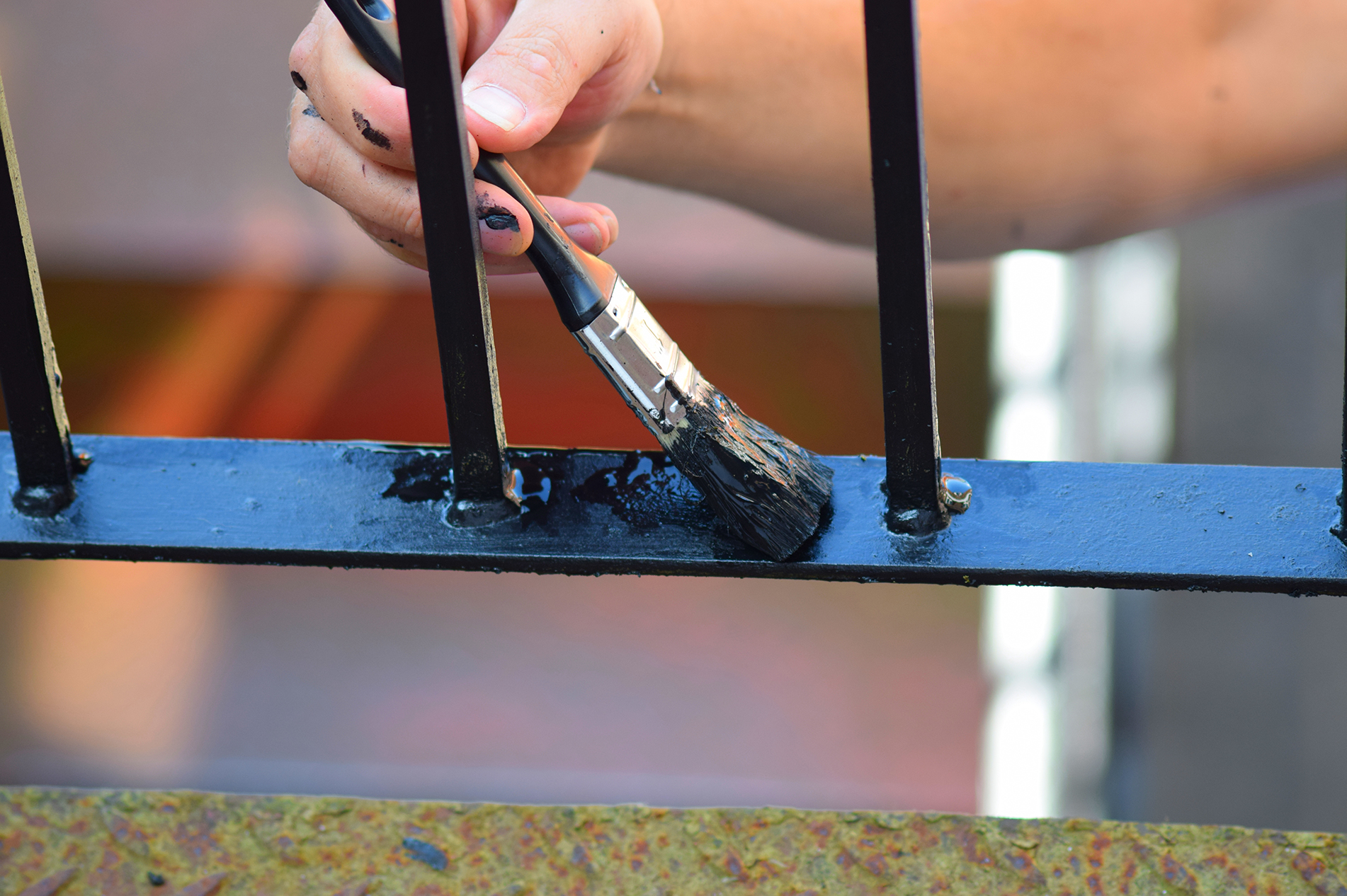 Close up photo of a brush painting an exterior metal railing.