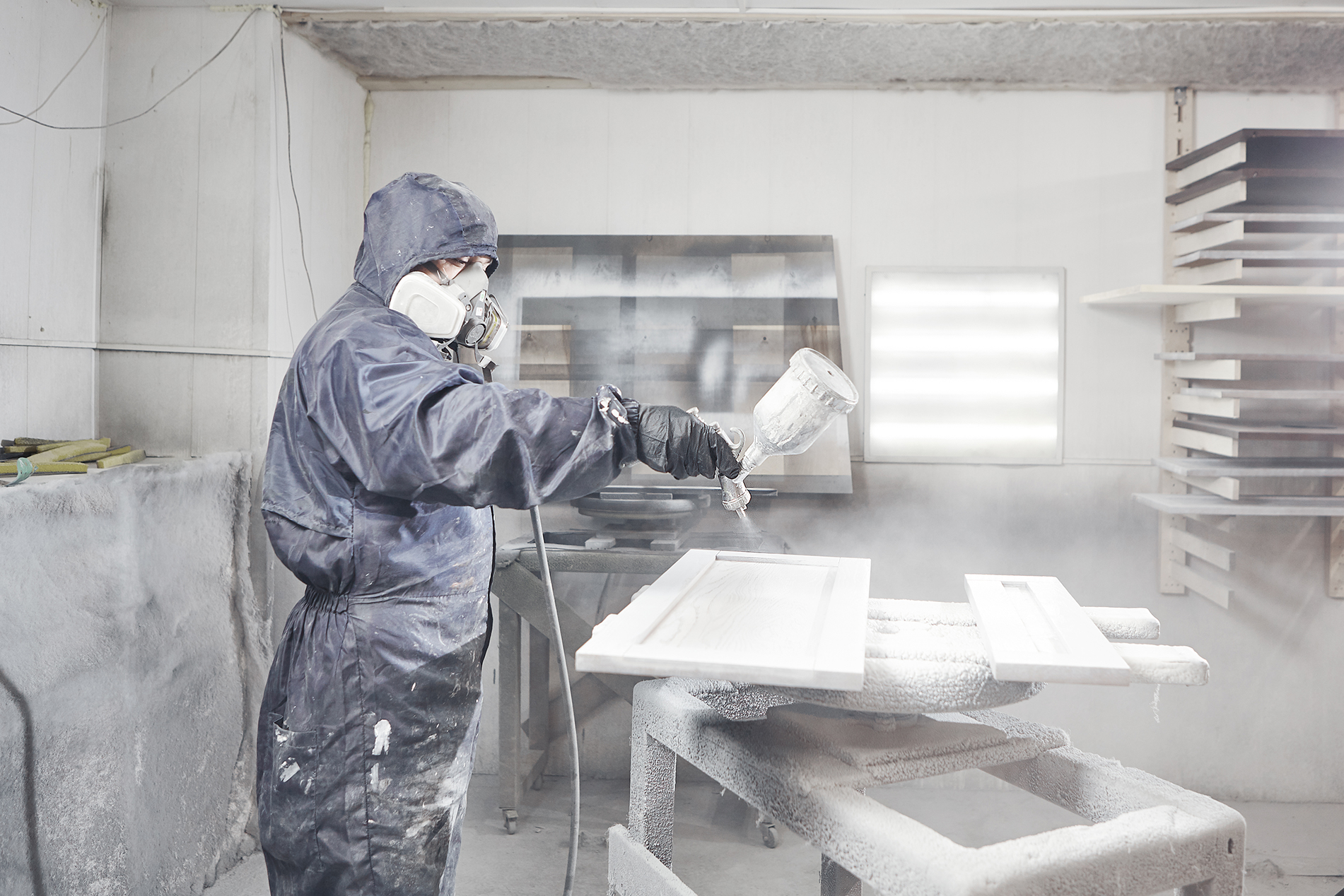 Worker spray painting a cabinet door in a spray room.