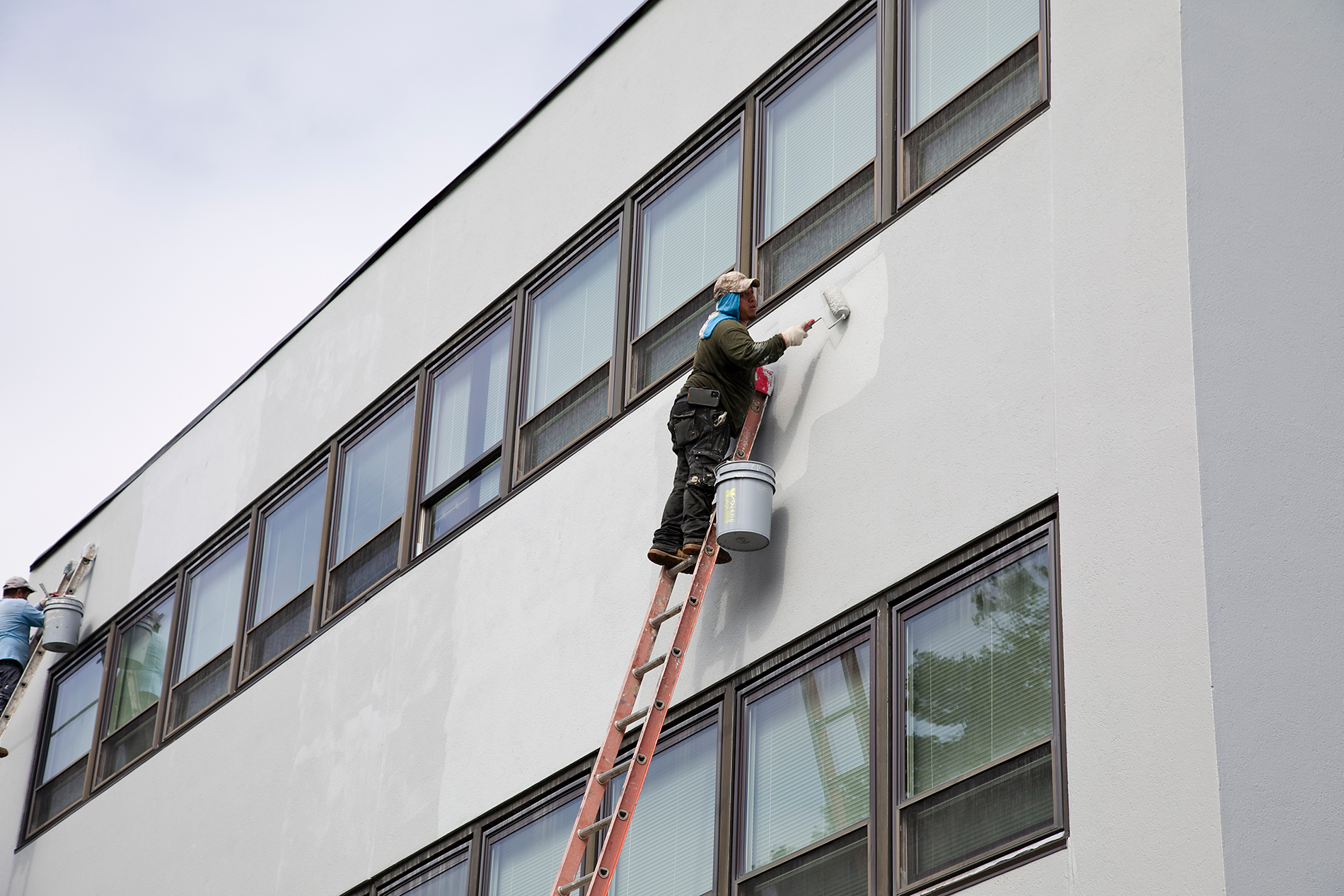 Worker painting a commercial buildings wall on an orange ladder.