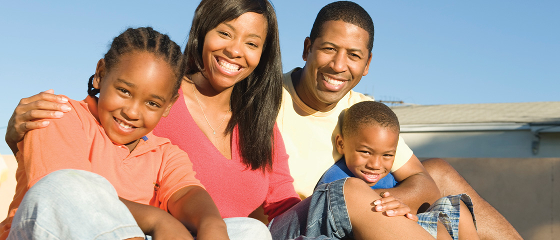 A smiling family of four sits closely together, representing strong relationships and community support around a charter school