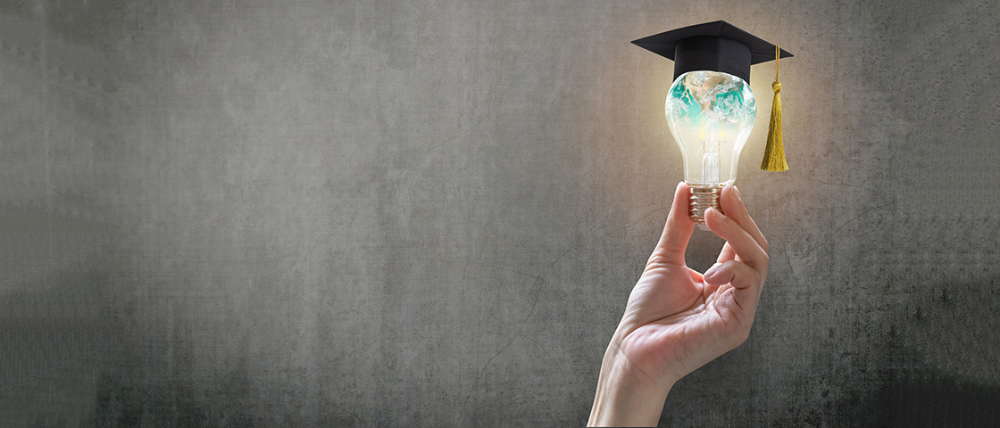 A hand holding a glowing lightbulb shaped like a globe with a graduation cap, symbolizing innovation in education.