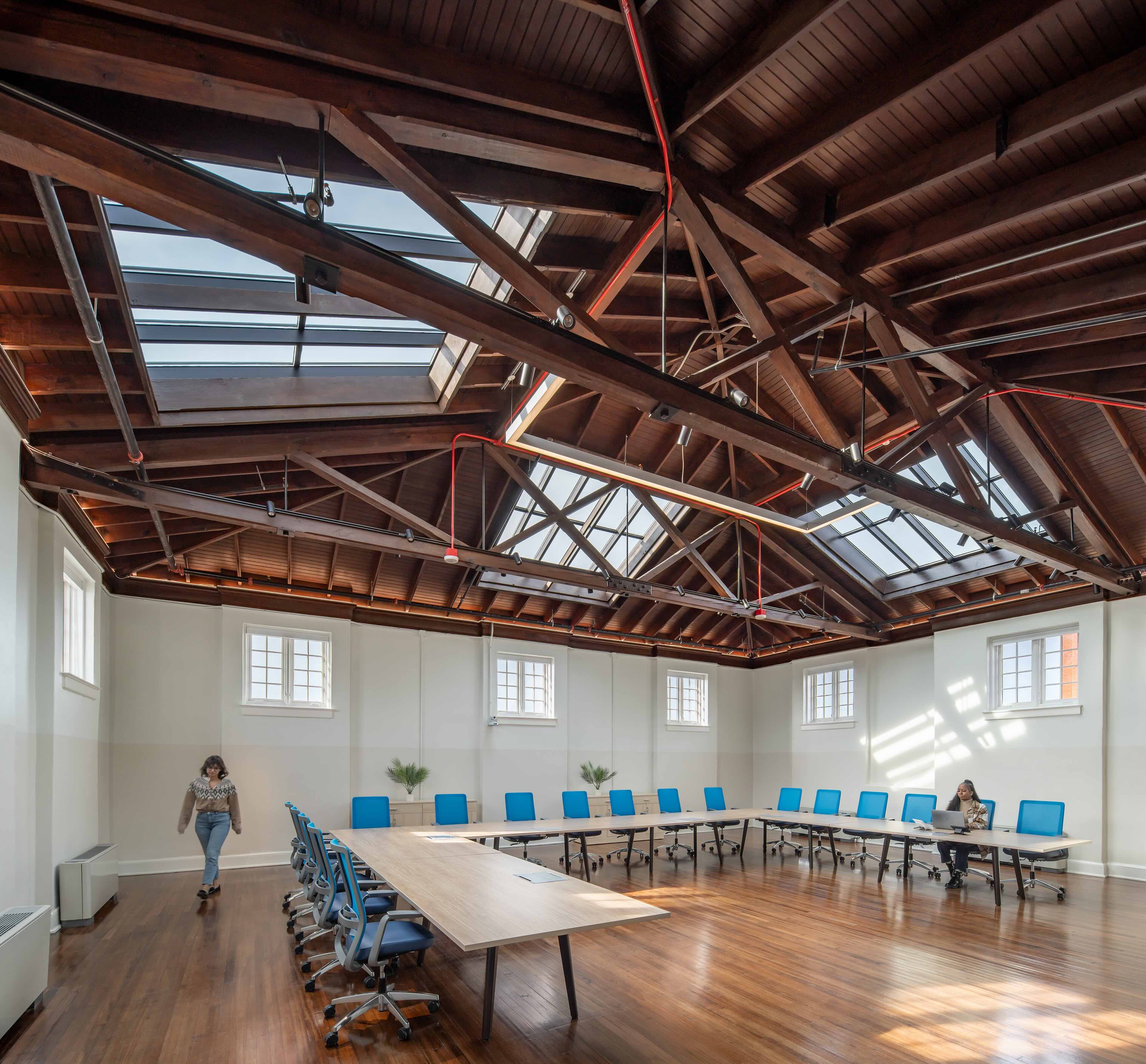 Woman walks through conference room; room features skylights and beams on the ceiling.