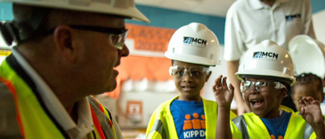 Children wearing safety vests and glasses learn STEM skills from a mentor at MCN Build, fostering education and community growth.
