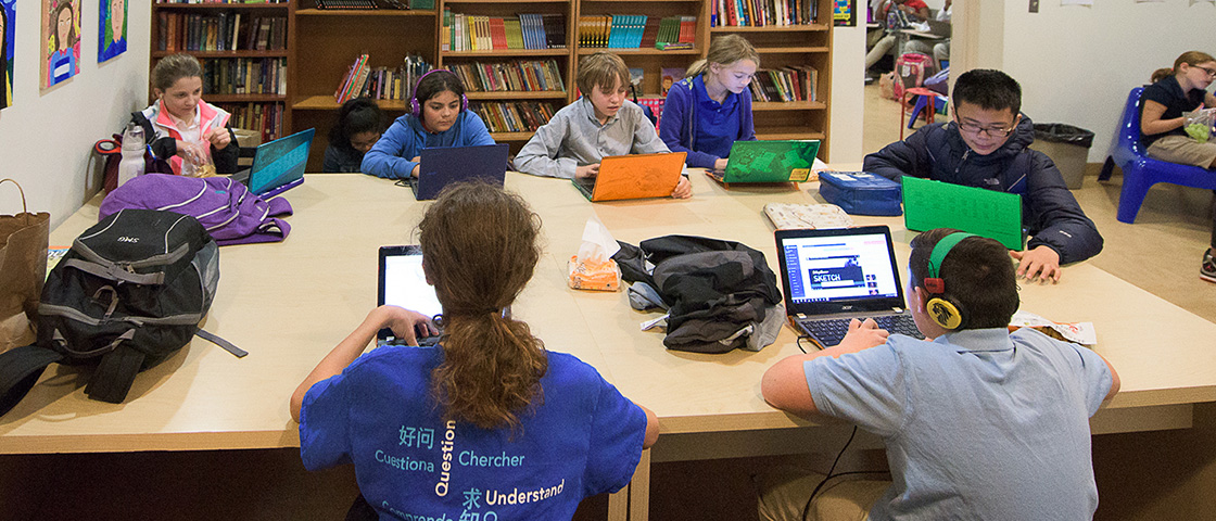 A group of children sitting around a table, each using a laptop, engaged in learning and collaborating.