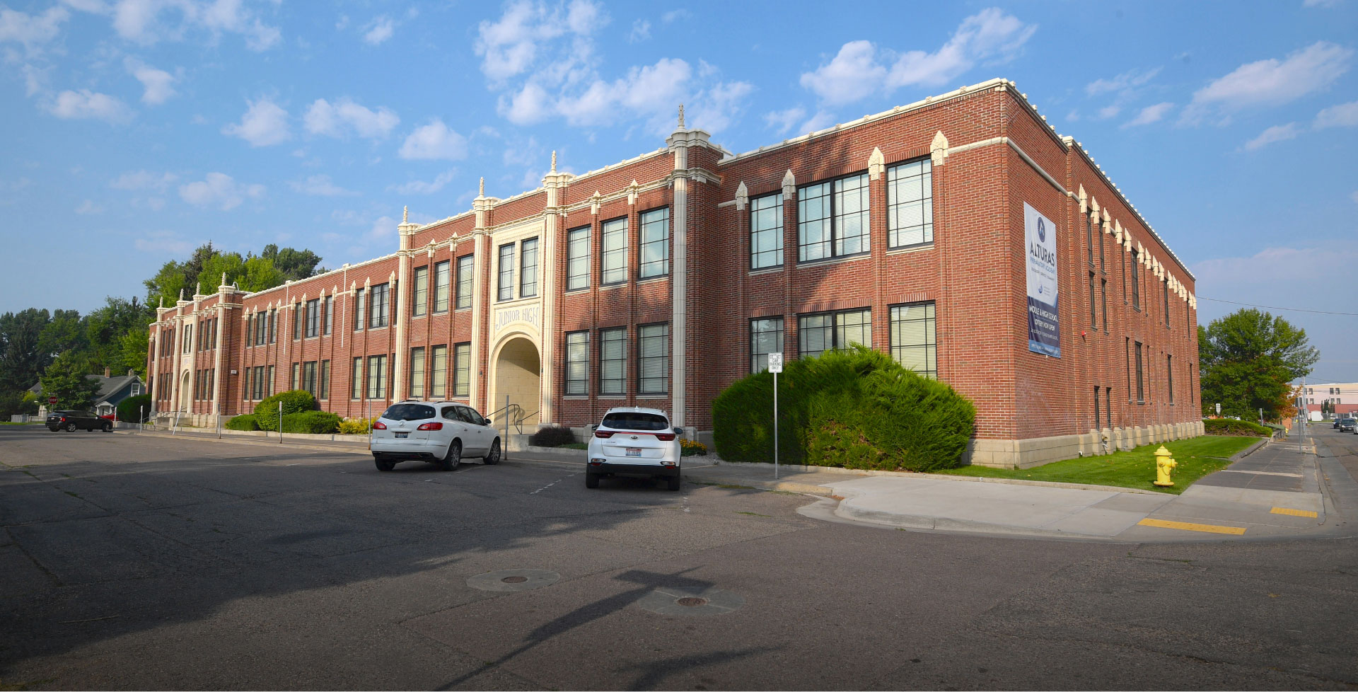 Two-story historic brick school building with arched entrance on a quiet street under blue sky.