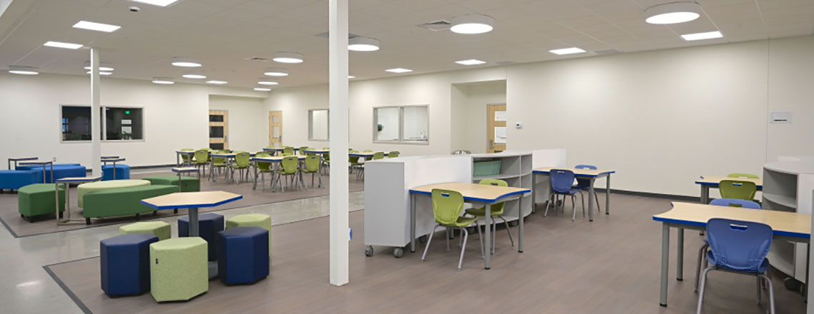 Open, modern learning space with flexible tables, green and blue seating, and bright overhead lighting.