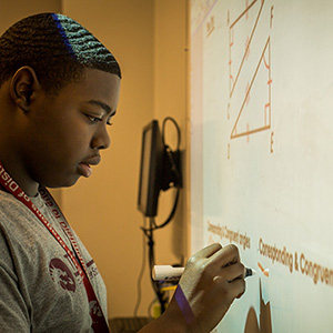 Student focused on writing math equations on an interactive whiteboard during class.