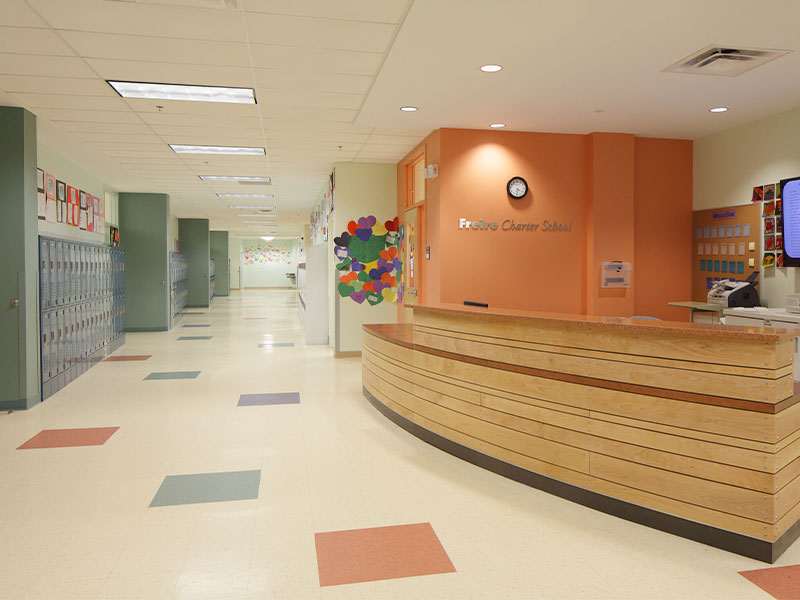 Bright school hallway with lockers, colorful artwork, and a reception desk at Freire Charter School.