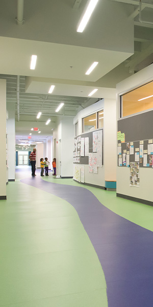 Modern school hallway with colorful curved flooring, student artwork, and children walking with a teacher.