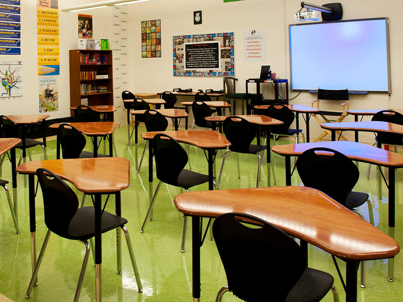 Classroom with green floors, triangular desks, a whiteboard, bookshelves, and colorful posters.