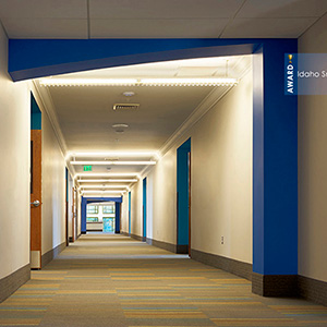 Bright, modern hallway with blue and beige walls, overhead lighting, and a patterned carpet. Signs indicate an award-winning design in Idaho.