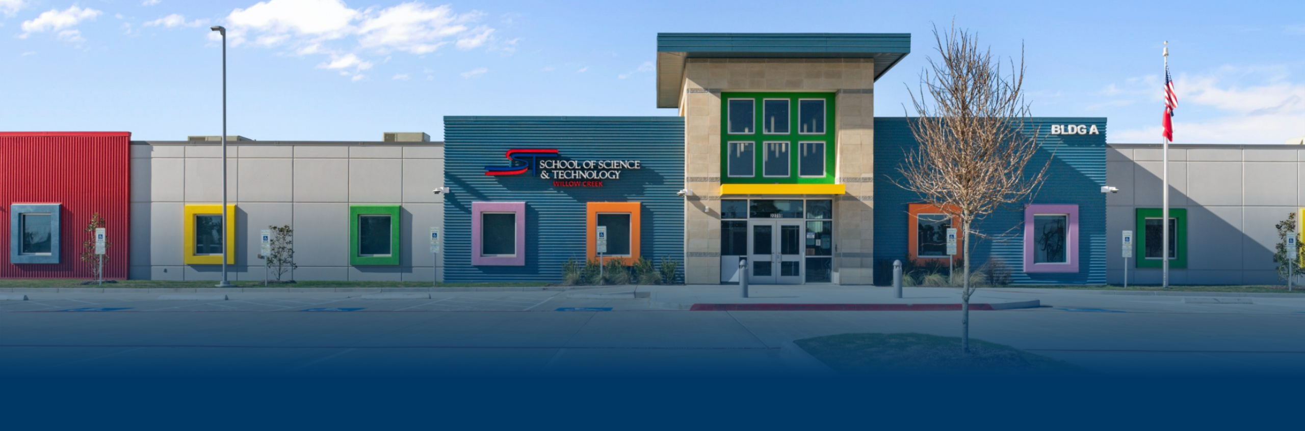 Modern school building with colorful square windows and a central glass entrance. The facade includes vibrant red, blue, and yellow accents.