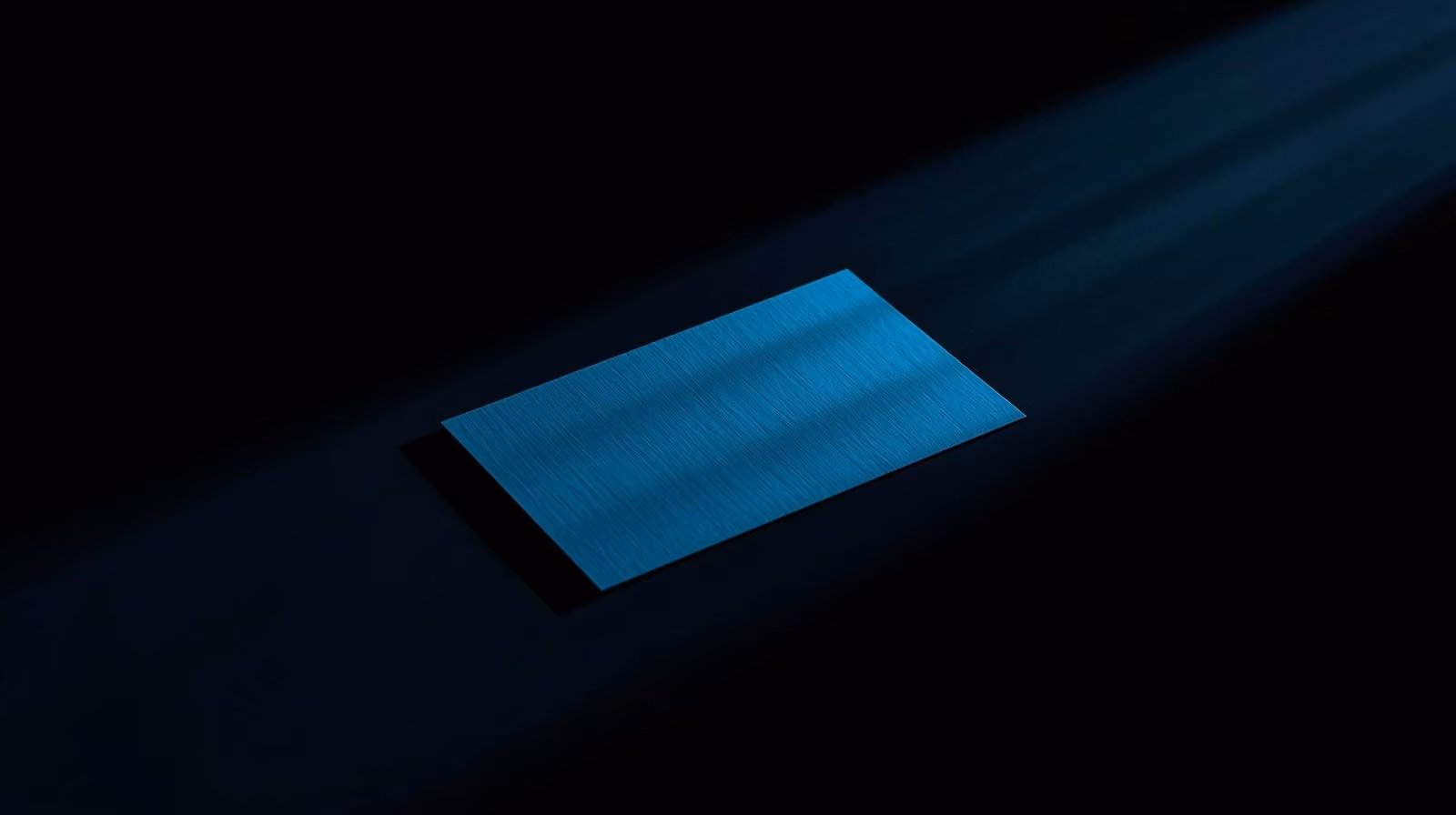 Blue textured rectangular card illuminated by a narrow beam of light on a dark background.
