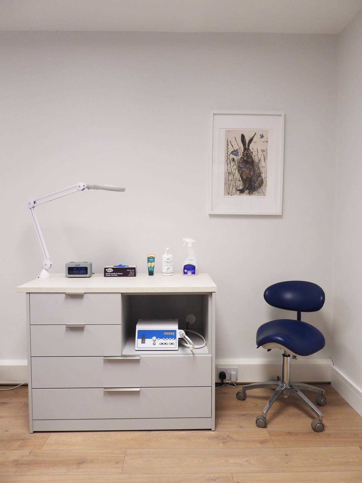 Treatment room storage at Kenmare Foot Clinic, with clinical equipment, an adjustable lamp and a practitioner's stool.