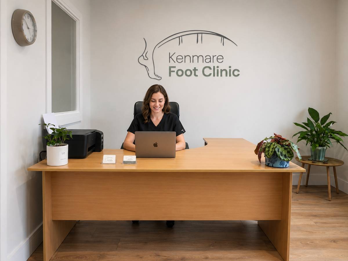 The reception area at Kenmare Foot Clinic, with a wooden desk and the clinic's logo on the wall.