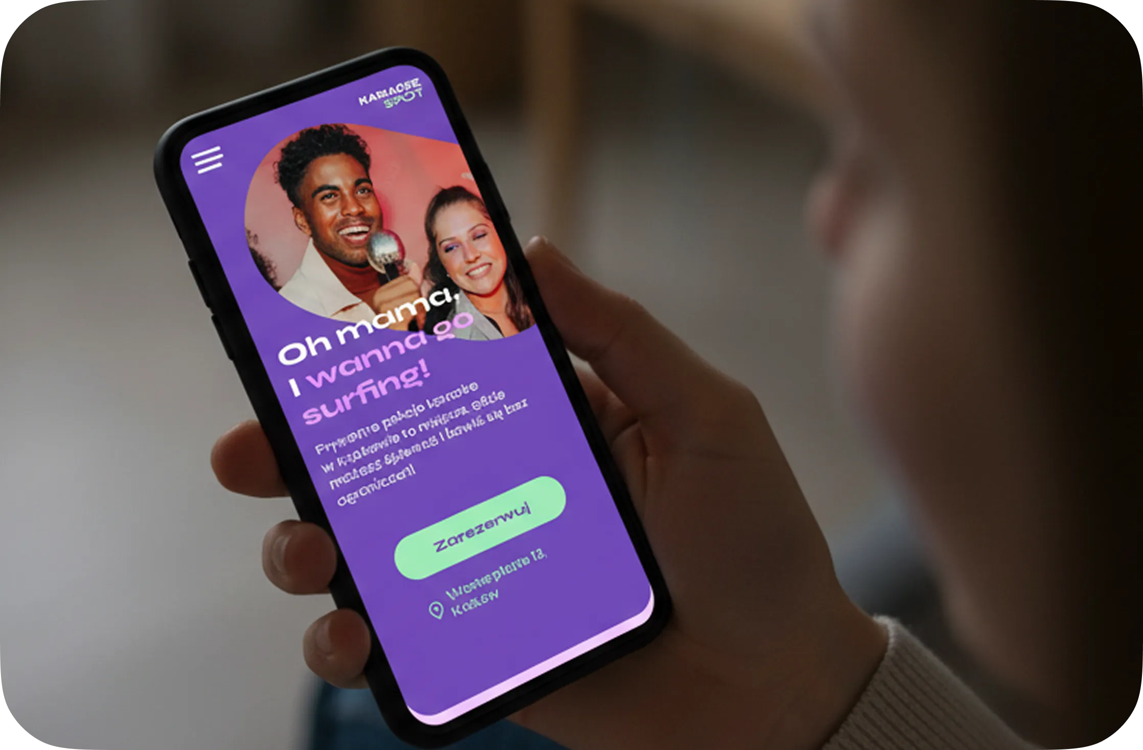 Person holding a smartphone displaying a Karaoke Spot homepage with a photo of two people singing karaoke and text saying 'Oh mama, I wanna go surfing!'