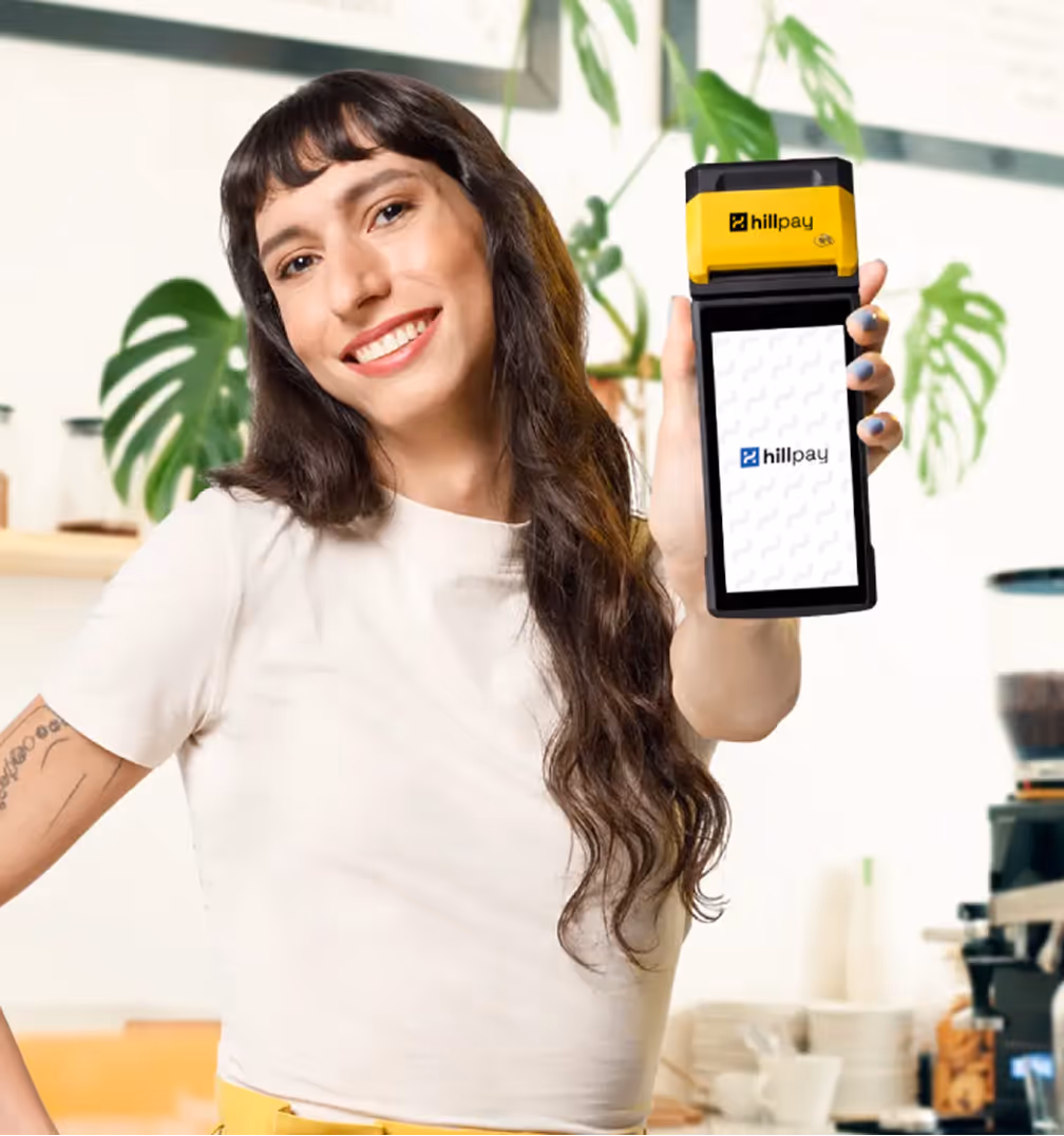 Mulher sorridente segura uma maquininha Hillpay Smart em um ambiente de cafeteria moderno.
