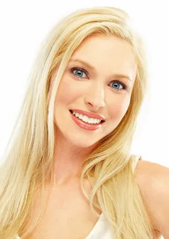 A smiling person with long blonde hair and blue eyes looks towards the camera