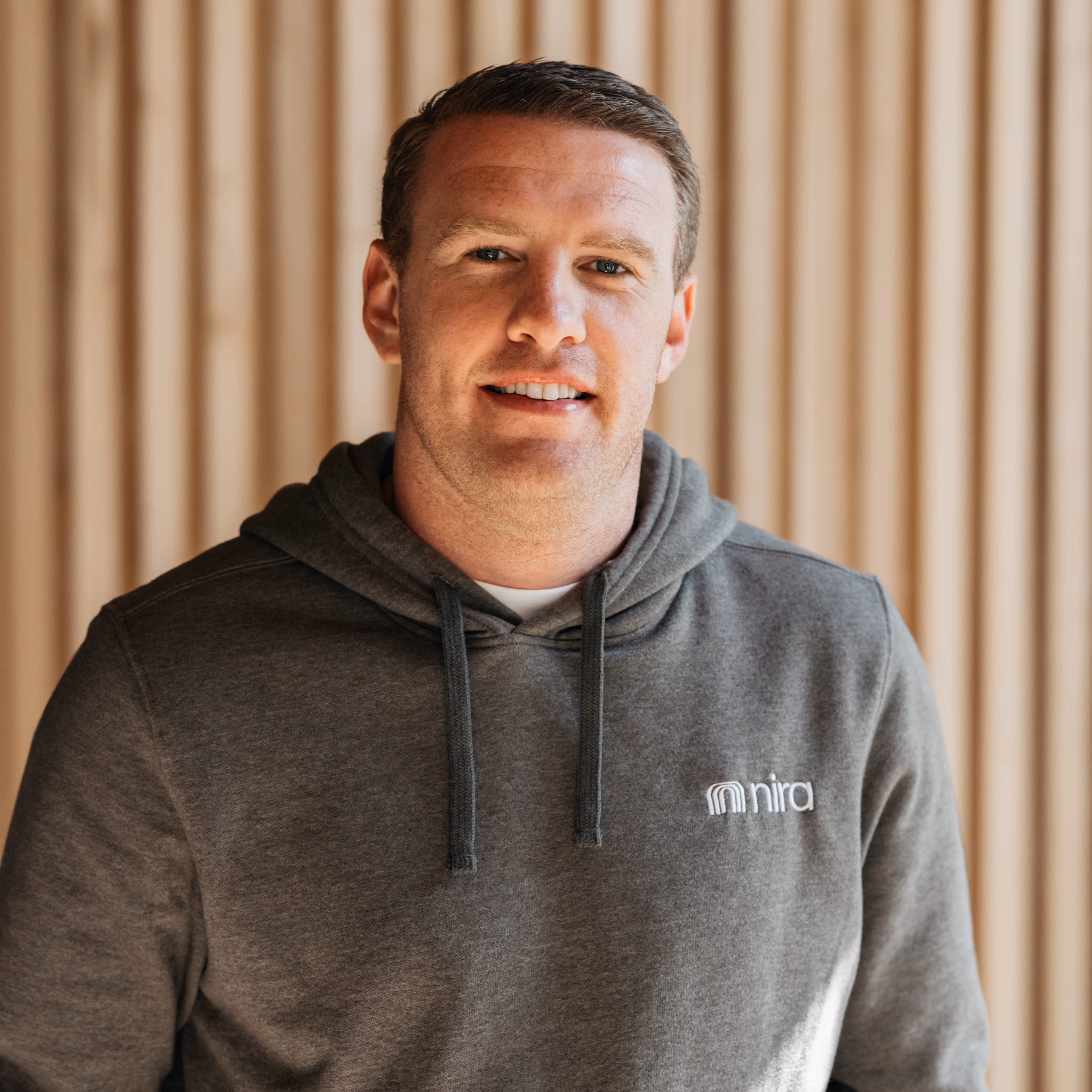 A man in a Nira Health hoodie in front of a wood wall. 