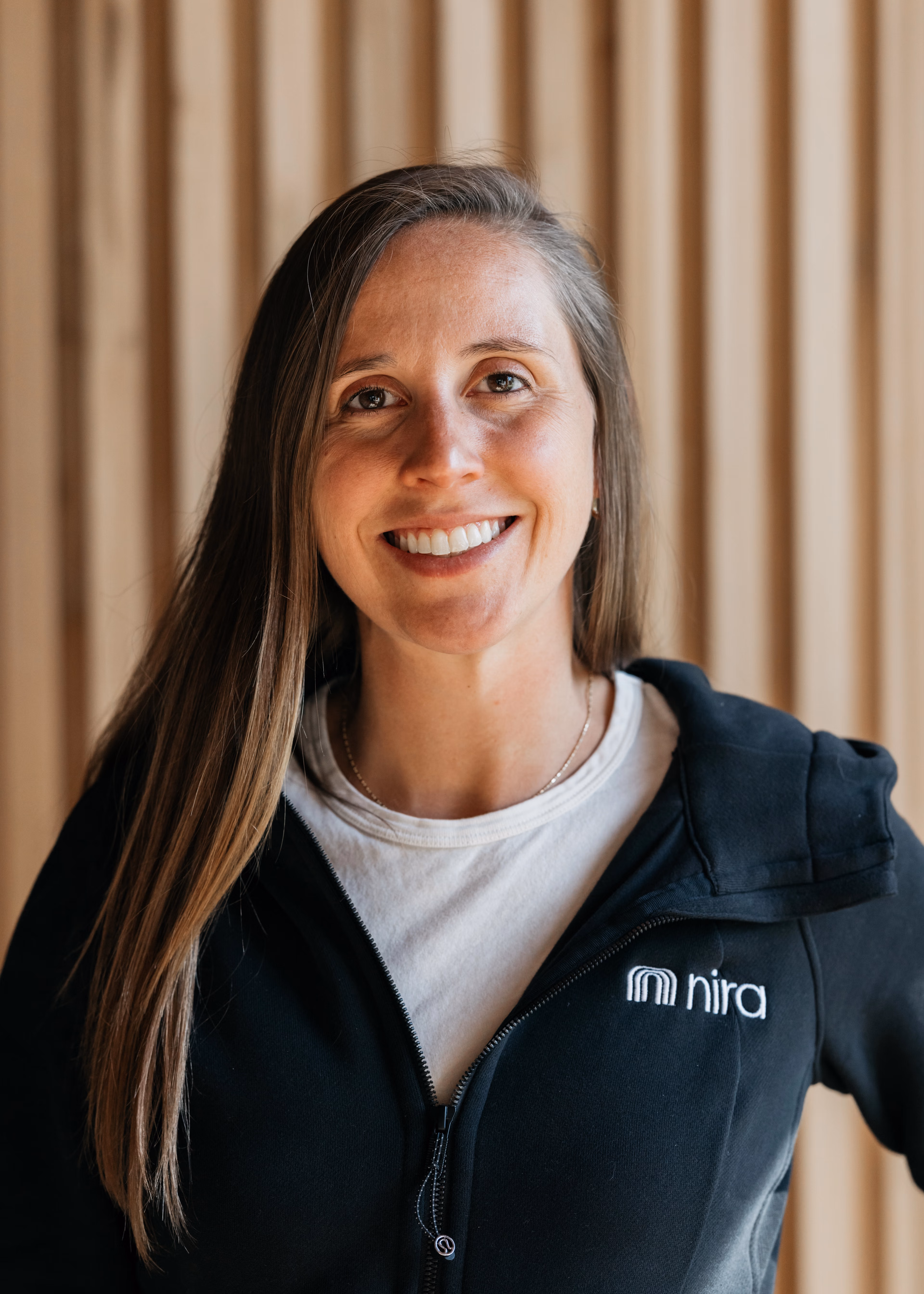 Gracia Steen in a Nira Health jacket in front of a wood wall. 
