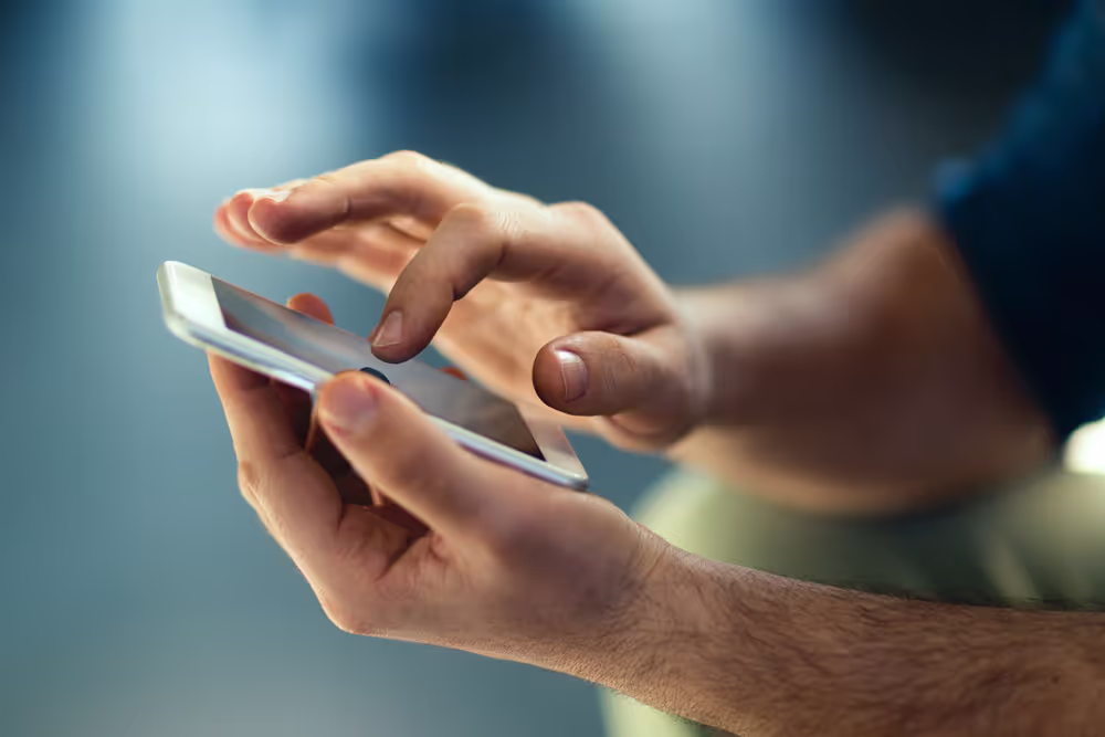Close-up of a person using a white smartphone with one hand holding and the other hand tapping the screen.