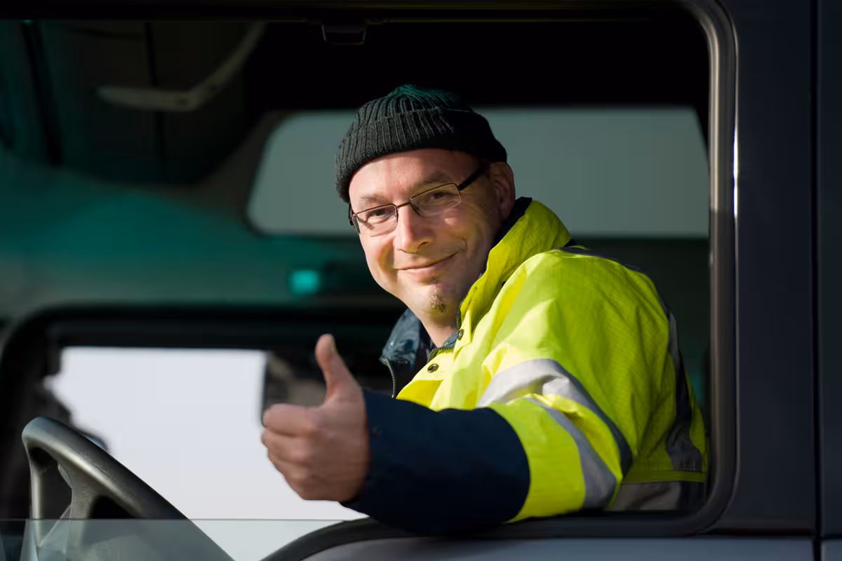 Truck driver in a safety jacket giving a thumbs up.