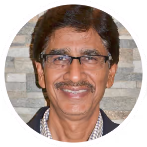 Portrait of a middle-aged man with glasses, mustache, and short dark hair smiling in front of a stone wall.