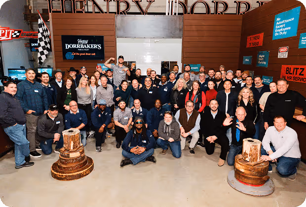 Large group of diverse people posing together indoors with wooden chess pieces and multiple signs on the walls.