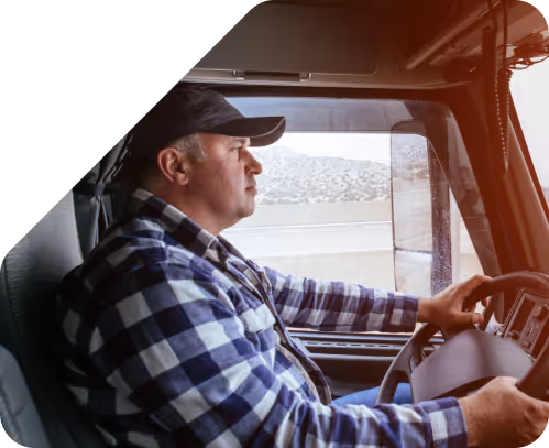 Man wearing a black cap and checkered shirt driving a truck on a highway.