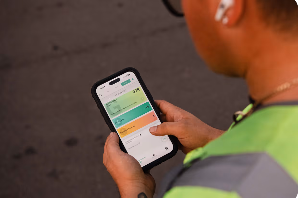 Person in green and gray jacket holding smartphone displaying a dashboard with green, teal, and orange sections showing performance metrics.