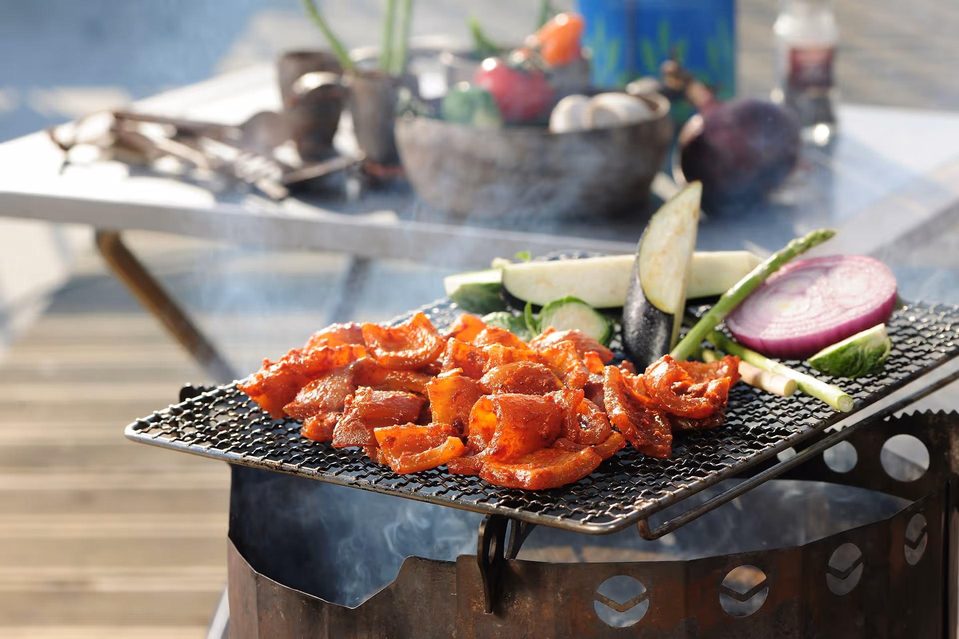 Spicy marinated meat and assorted vegetables grilling on a mesh grill over an outdoor fire pit.