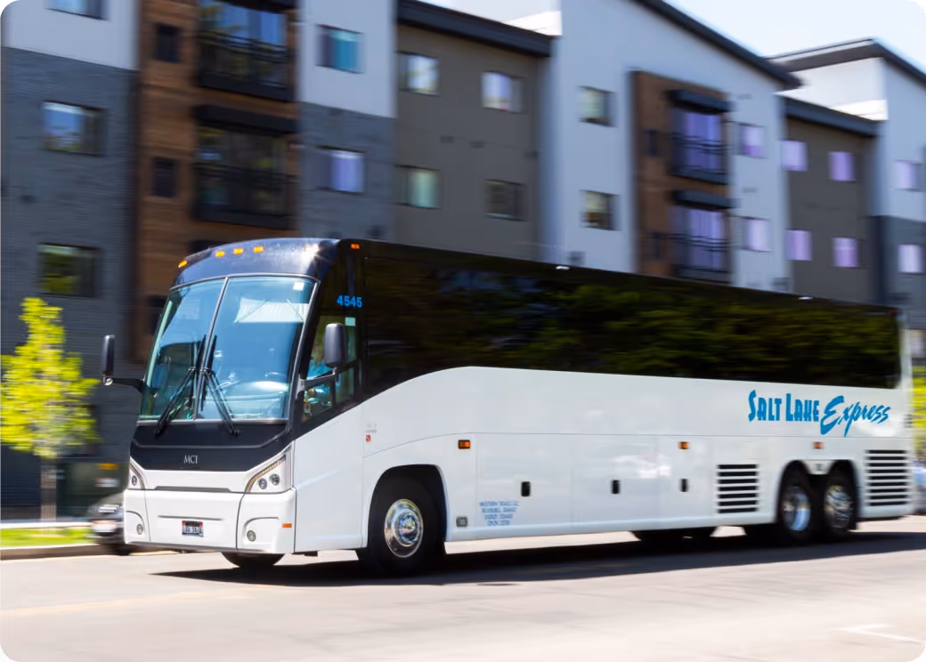 White and black Salt Lake Express coach bus moving on a city street with apartment buildings in the background.