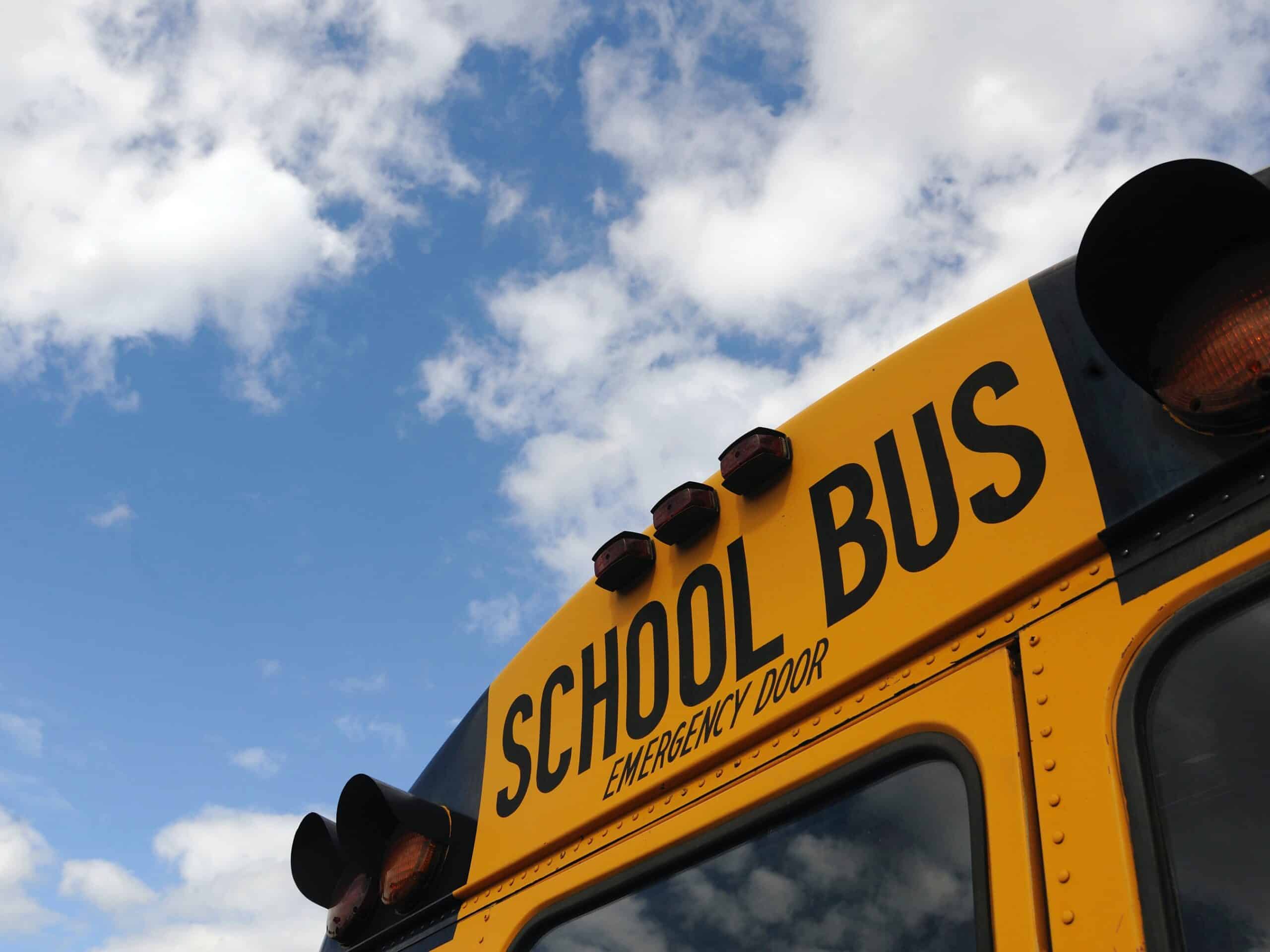 Rear roofline of a yellow school bus with emergency door label and warning lights against a cloudy sky
