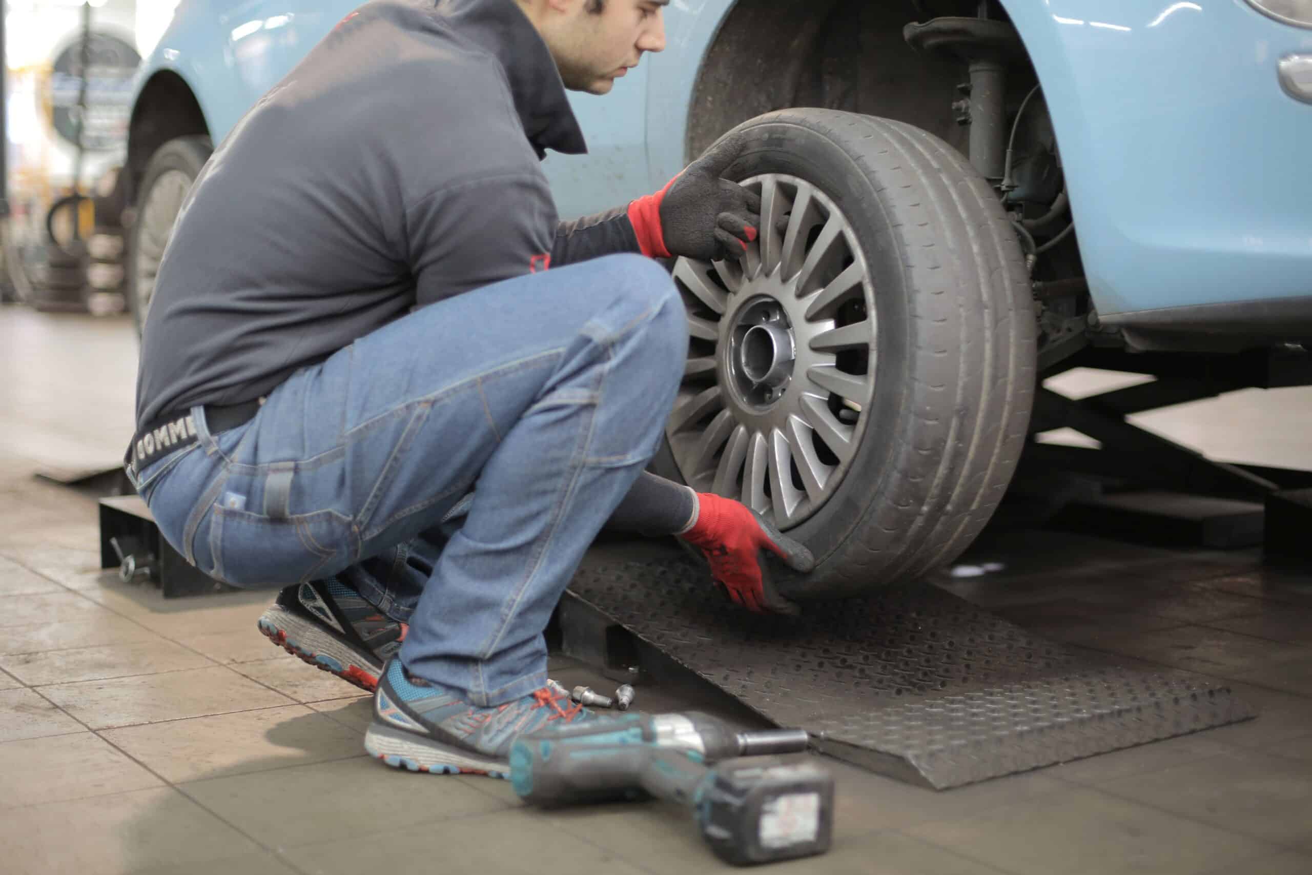Mechanic in red gloves crouching to inspect a tire on a blue car raised on a workshop lift