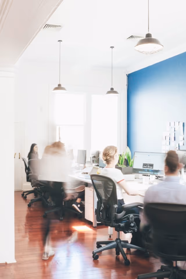 Modern office with people working at desks and one person walking past in motion blur.