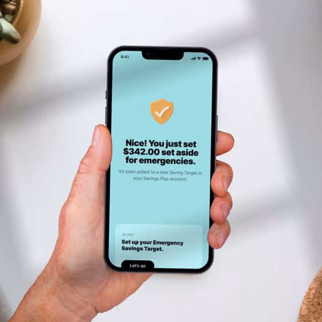 Hand holding smartphone displaying a confirmation screen for setting aside $342.00 for emergency savings.