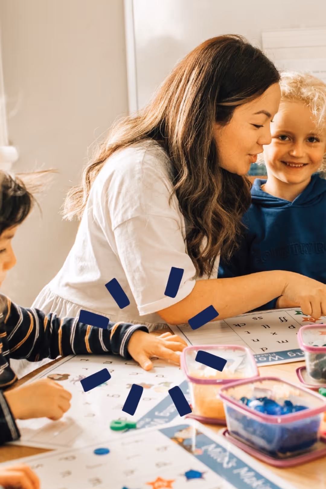 A woman and two children working together at a table on a learning activity with letter and number cards.