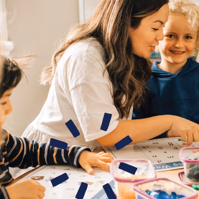 A woman and two children engaged in a learning activity at a table with educational materials.