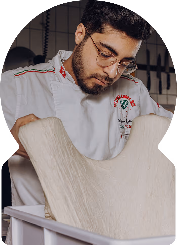 Chef in white uniform shaping pizza dough in a kitchen.