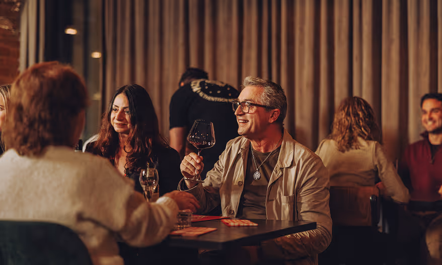 Man and woman smiling and holding wine glasses while sitting at a restaurant table.